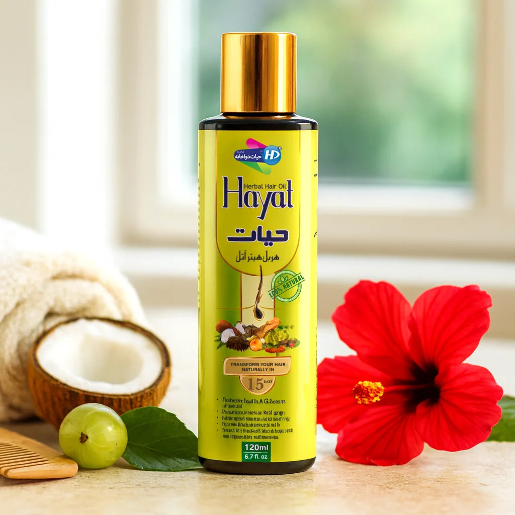 Hayat Herbal Hair Oil bottle with golden cap placed near coconut half, hibiscus flower, amla fruit, and a wooden comb in a softly lit room.