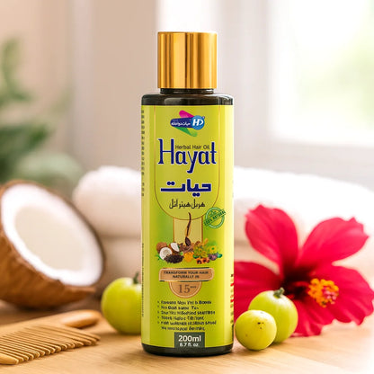 Hayat Herbal Hair Oil bottle with golden cap displayed beside coconut, hibiscus flower, amla fruit, and wooden comb on a bright indoor background.