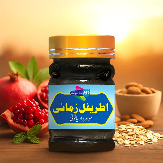 Itrefal Zamani jar with golden lid placed beside pomegranate, almonds, oats, and mint on a wooden table.