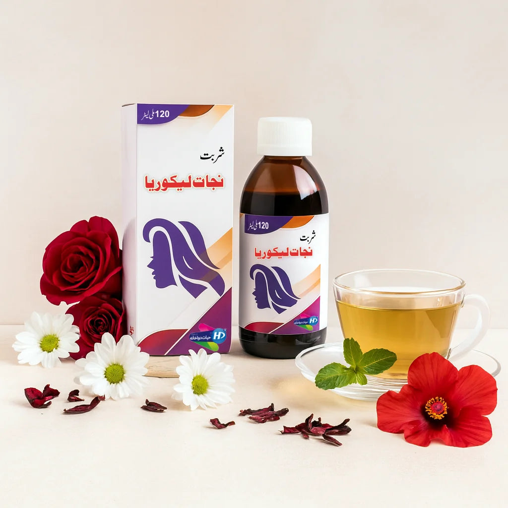 Sharbat Nijat-e-Likoria bottle and box placed with roses, daisies, hibiscus petals, and a cup of herbal tea.