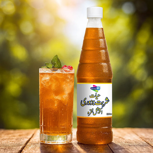 Sharbat Bazoori bottle beside a chilled glass of herbal drink with mint and berries, photographed outdoors in natural sunlight.