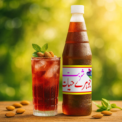 Sharbat Johar-e-Hayat bottle beside a glass of iced red drink topped with almonds and mint leaves, with almonds scattered on the wooden table in natural sunlight.